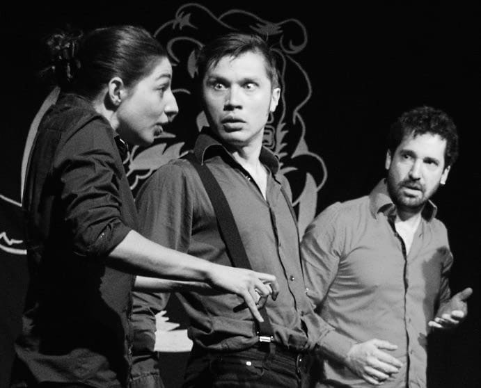 Three improvisers on stage reacting intensely to each other, each showing a distinct emotional expression in the moment.
